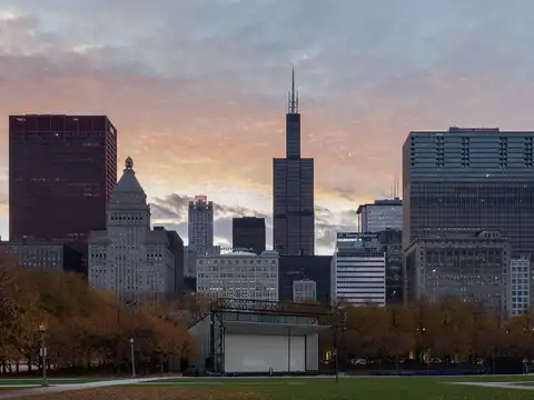 The Chicago skyline at dusk seen across Grant Park, with the Willis Tower and its aerials at the centre and autumn trees in the foreground.